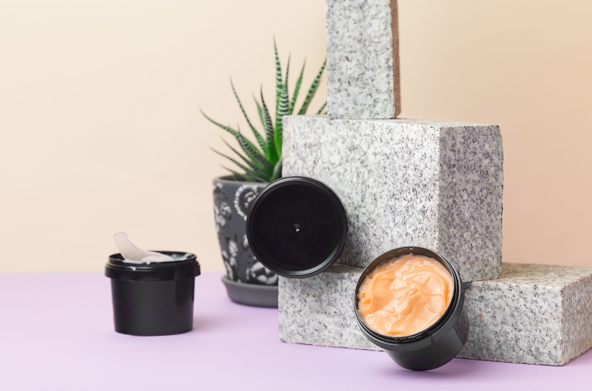 Natural products for body and face skin care. Variants of cream in black jars on a granite brick and beige background